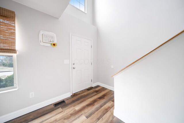 entryway featuring visible vents, baseboards, stairway, a towering ceiling, and wood finished floors