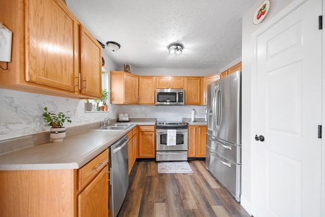 kitchen featuring dark wood finished floors, a sink, decorative backsplash, light countertops, and appliances with stainless steel finishes