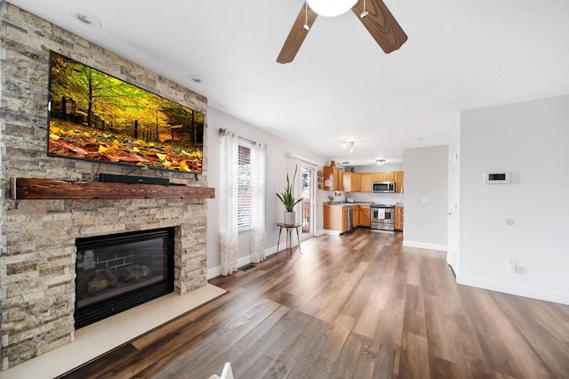 unfurnished living room with a stone fireplace, a ceiling fan, dark wood-type flooring, and baseboards