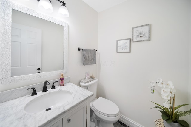 half bathroom featuring toilet, vanity, and baseboards