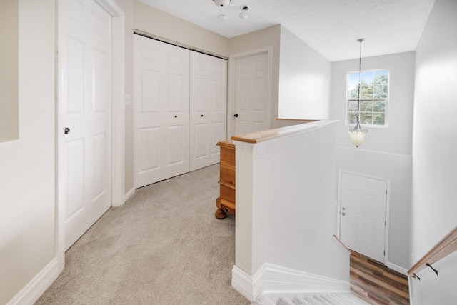 corridor with an upstairs landing, light colored carpet, and baseboards