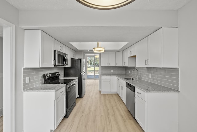 kitchen with light stone counters, light wood-style flooring, a sink, appliances with stainless steel finishes, and white cabinetry