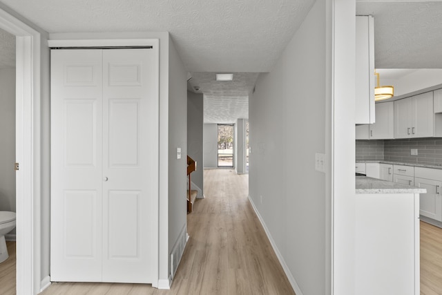 corridor with visible vents, light wood-style flooring, a textured ceiling, and baseboards