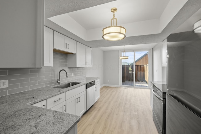 kitchen featuring a tray ceiling, stainless steel appliances, decorative backsplash, a sink, and light wood-style floors