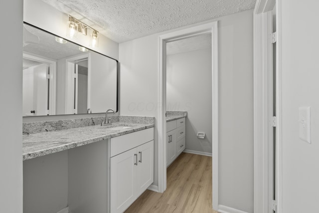 bathroom with baseboards, a textured ceiling, wood finished floors, and vanity