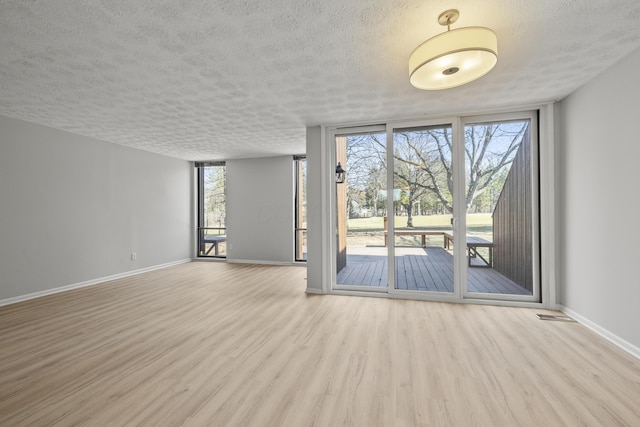 empty room featuring plenty of natural light, expansive windows, baseboards, and wood finished floors