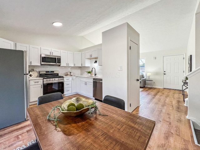 kitchen with a sink, tasteful backsplash, appliances with stainless steel finishes, light countertops, and lofted ceiling