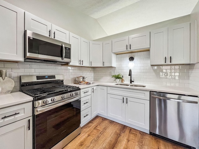 kitchen featuring light wood-type flooring, a sink, appliances with stainless steel finishes, light countertops, and lofted ceiling