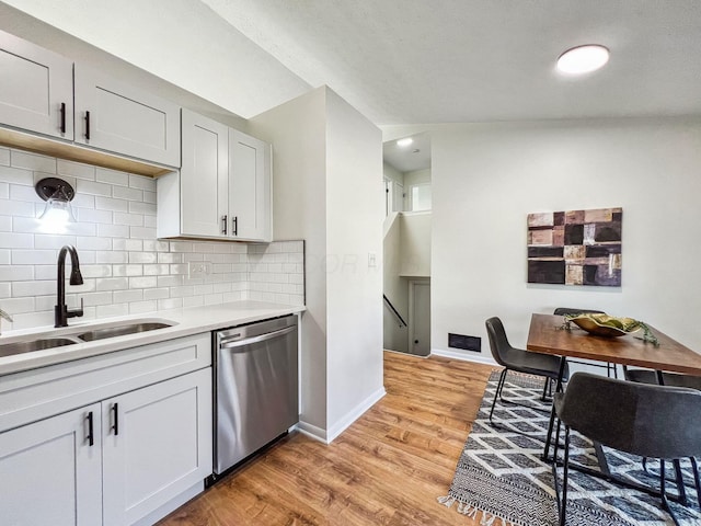 kitchen with light wood-type flooring, a sink, light countertops, dishwasher, and tasteful backsplash