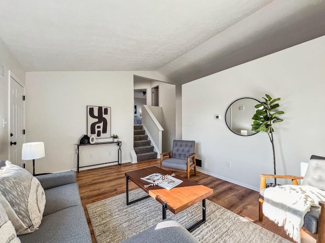 living room featuring vaulted ceiling, stairway, baseboards, and wood finished floors