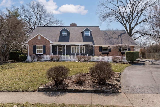 cape cod home with covered porch, a chimney, a front lawn, a fenced front yard, and brick siding