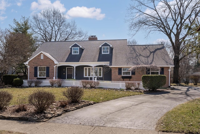 new england style home featuring brick siding, a porch, and a fenced front yard