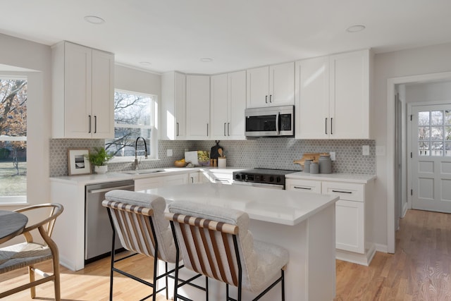 kitchen with a kitchen breakfast bar, stainless steel appliances, light wood-style floors, and a sink