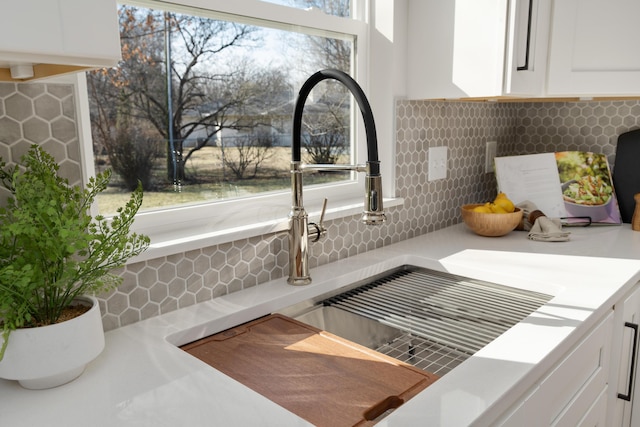 interior details with backsplash, white cabinets, light countertops, and a sink