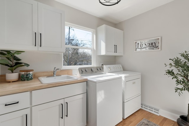 laundry area featuring visible vents, light wood-type flooring, washer and clothes dryer, a sink, and cabinet space