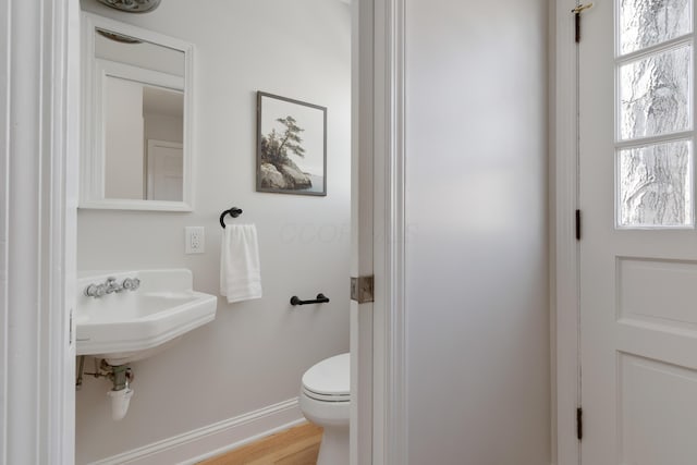 half bath with toilet, baseboards, and wood finished floors