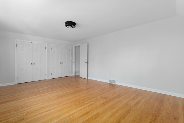 unfurnished bedroom with light wood finished floors, visible vents, and multiple closets