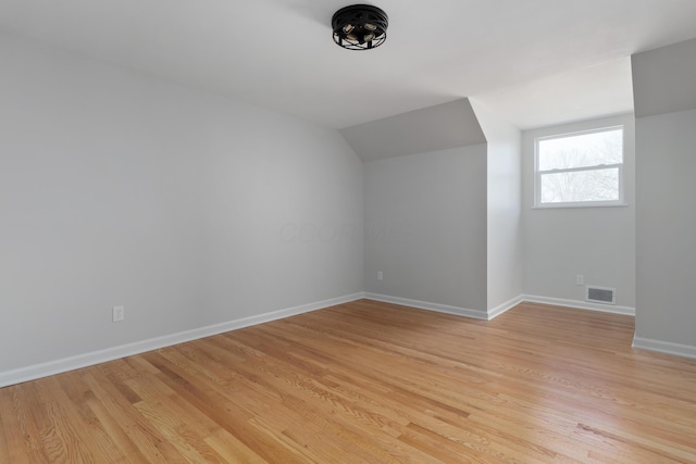 additional living space featuring light wood finished floors, visible vents, lofted ceiling, and baseboards