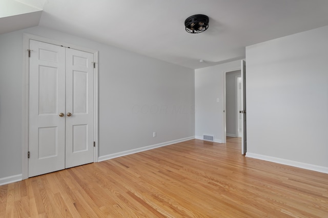 unfurnished bedroom featuring light wood finished floors, visible vents, lofted ceiling, and baseboards