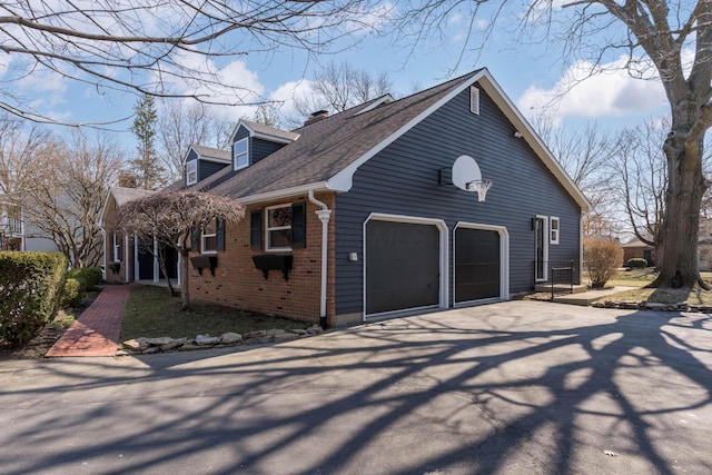 view of property exterior featuring brick siding, roof with shingles, a chimney, a garage, and driveway