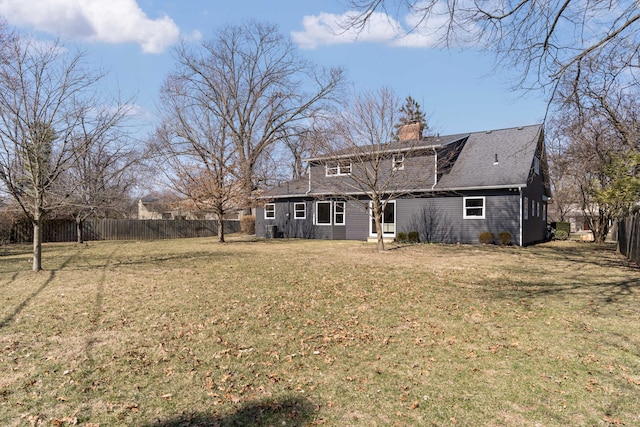 back of property with fence, a lawn, and a chimney