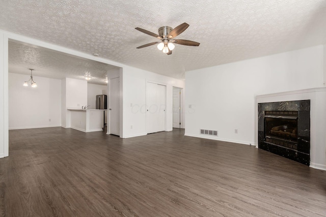 unfurnished living room with visible vents, dark wood-style flooring, a high end fireplace, a textured ceiling, and ceiling fan with notable chandelier