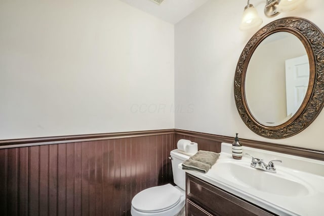 half bathroom featuring vanity, toilet, and wainscoting