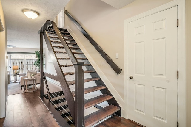 stairway featuring wood finished floors, baseboards, and a textured ceiling