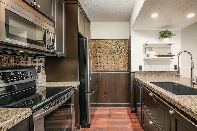 kitchen with a sink, a textured ceiling, dark wood finished floors, stainless steel appliances, and dark brown cabinets