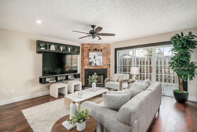 living room featuring wood finished floors, baseboards, a fireplace, ceiling fan, and a textured ceiling