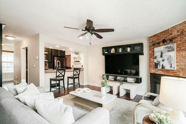 living area with a brick fireplace, baseboards, a ceiling fan, and wood finished floors