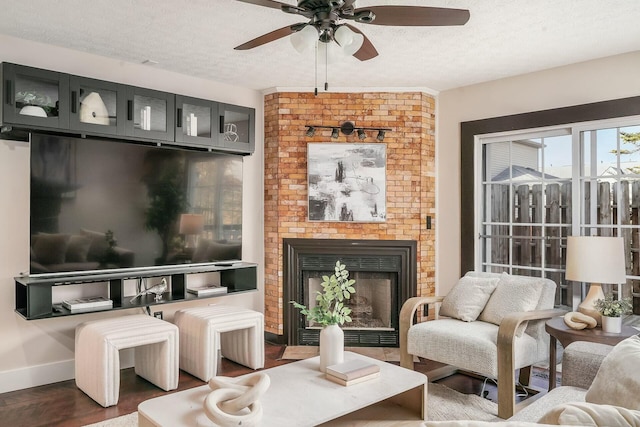 living area featuring a ceiling fan, a brick fireplace, wood finished floors, and a textured ceiling