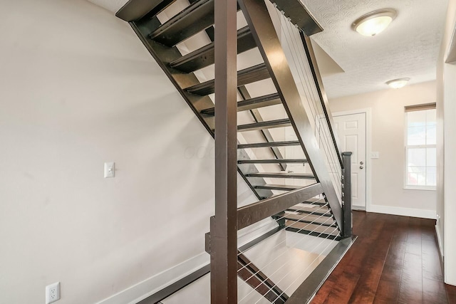 staircase featuring wood finished floors, baseboards, and a textured ceiling