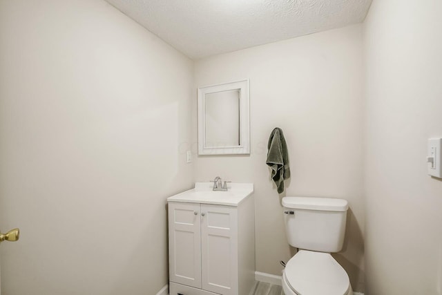 half bathroom with baseboards, toilet, vanity, and a textured ceiling