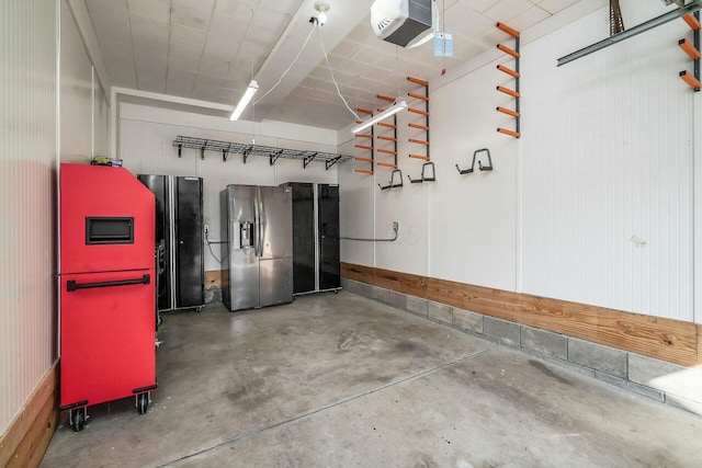 garage featuring a garage door opener, stainless steel fridge with ice dispenser, and freestanding refrigerator