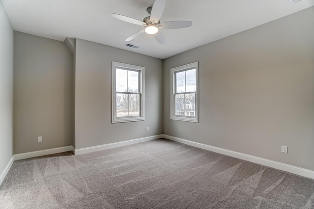 carpeted spare room with visible vents, baseboards, and ceiling fan