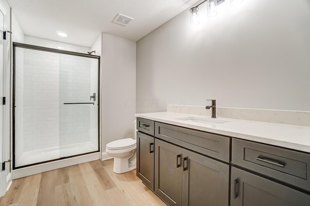 bathroom with visible vents, toilet, a stall shower, wood finished floors, and vanity