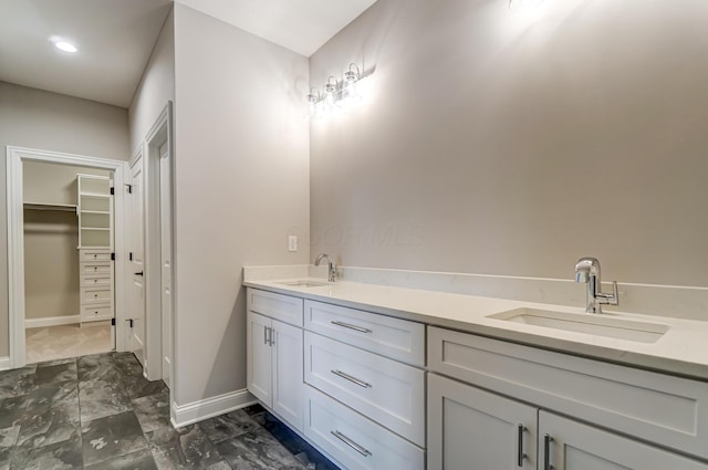 bathroom featuring double vanity, a spacious closet, baseboards, and a sink