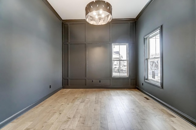 spare room with light wood finished floors, a decorative wall, baseboards, and visible vents