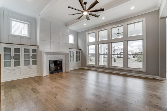 unfurnished living room with wood finished floors, beam ceiling, a high ceiling, ceiling fan, and a brick fireplace