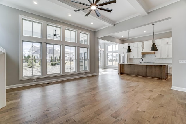 unfurnished living room with baseboards, beam ceiling, a ceiling fan, and light wood finished floors