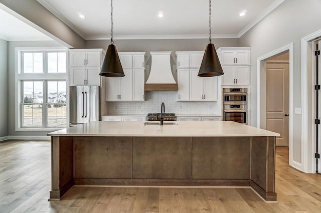 kitchen featuring a spacious island, custom exhaust hood, a sink, light countertops, and appliances with stainless steel finishes