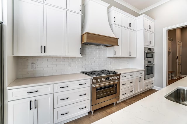 kitchen featuring white cabinetry, appliances with stainless steel finishes, ornamental molding, and custom range hood