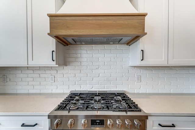 kitchen featuring custom exhaust hood, white cabinets, stove, and backsplash