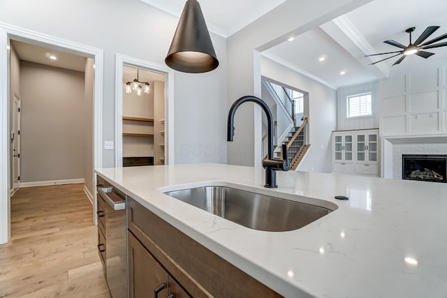 kitchen with a brick fireplace, ornamental molding, light wood-type flooring, and a sink