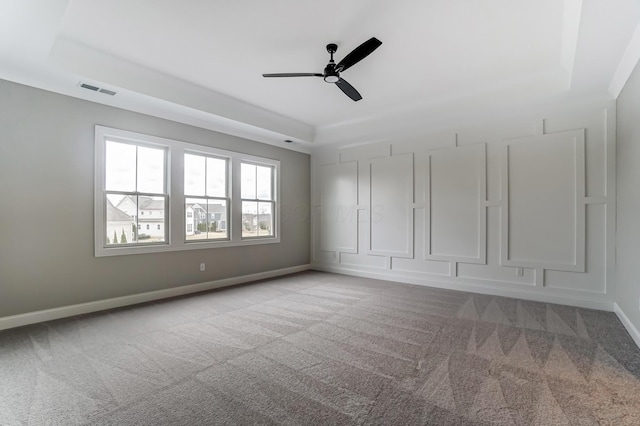 carpeted empty room featuring visible vents, ceiling fan, a raised ceiling, and baseboards