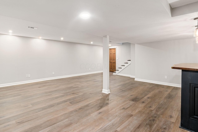 finished basement with visible vents, baseboards, stairway, recessed lighting, and wood finished floors