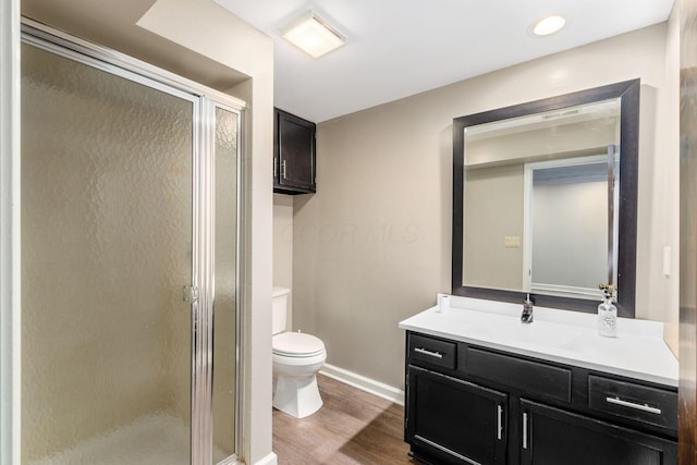 bathroom featuring toilet, wood finished floors, a shower stall, baseboards, and vanity