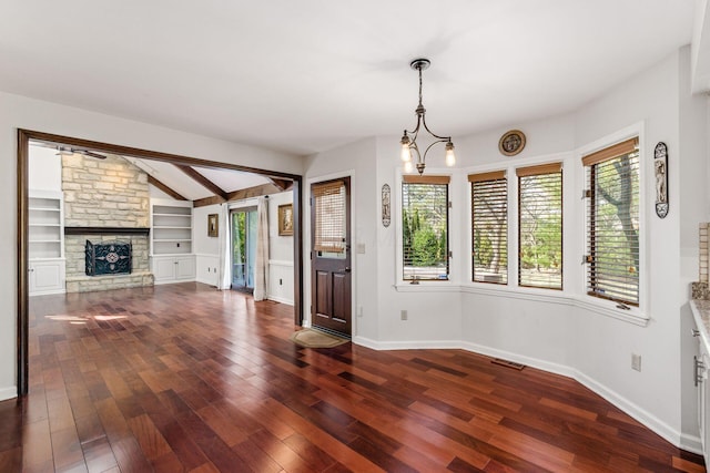 unfurnished dining area featuring lofted ceiling with beams, baseboards, dark wood-type flooring, and a fireplace