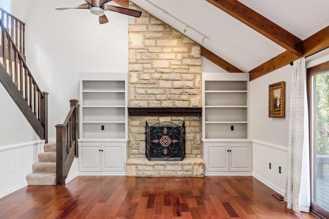 unfurnished living room with dark wood finished floors, a stone fireplace, built in shelves, and a wainscoted wall